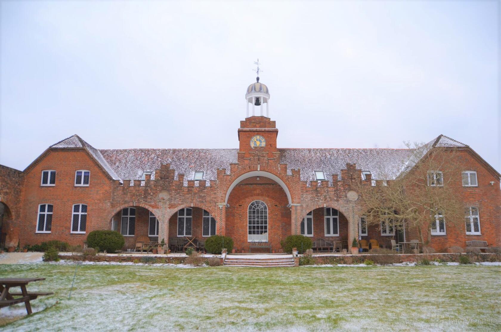 A brick event venue with arched windows, a central cupola, and snowy grounds at Rownhams House.