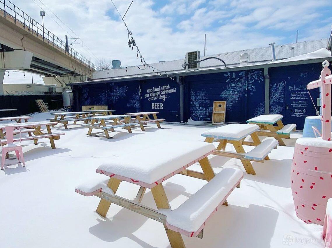 An outdoor bar area with snow-covered picnic tables, string lights, and mural walls at Celestial Beerworks.