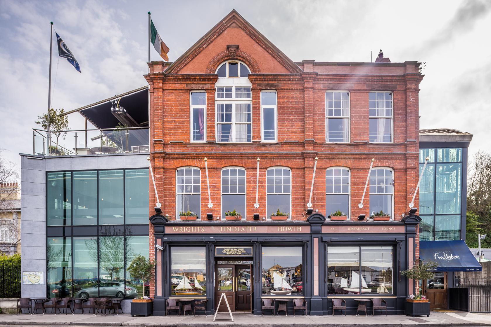 A brick restaurant facade with large windows, a glass extension, and outdoor seating at Wrights Findlater Howth.