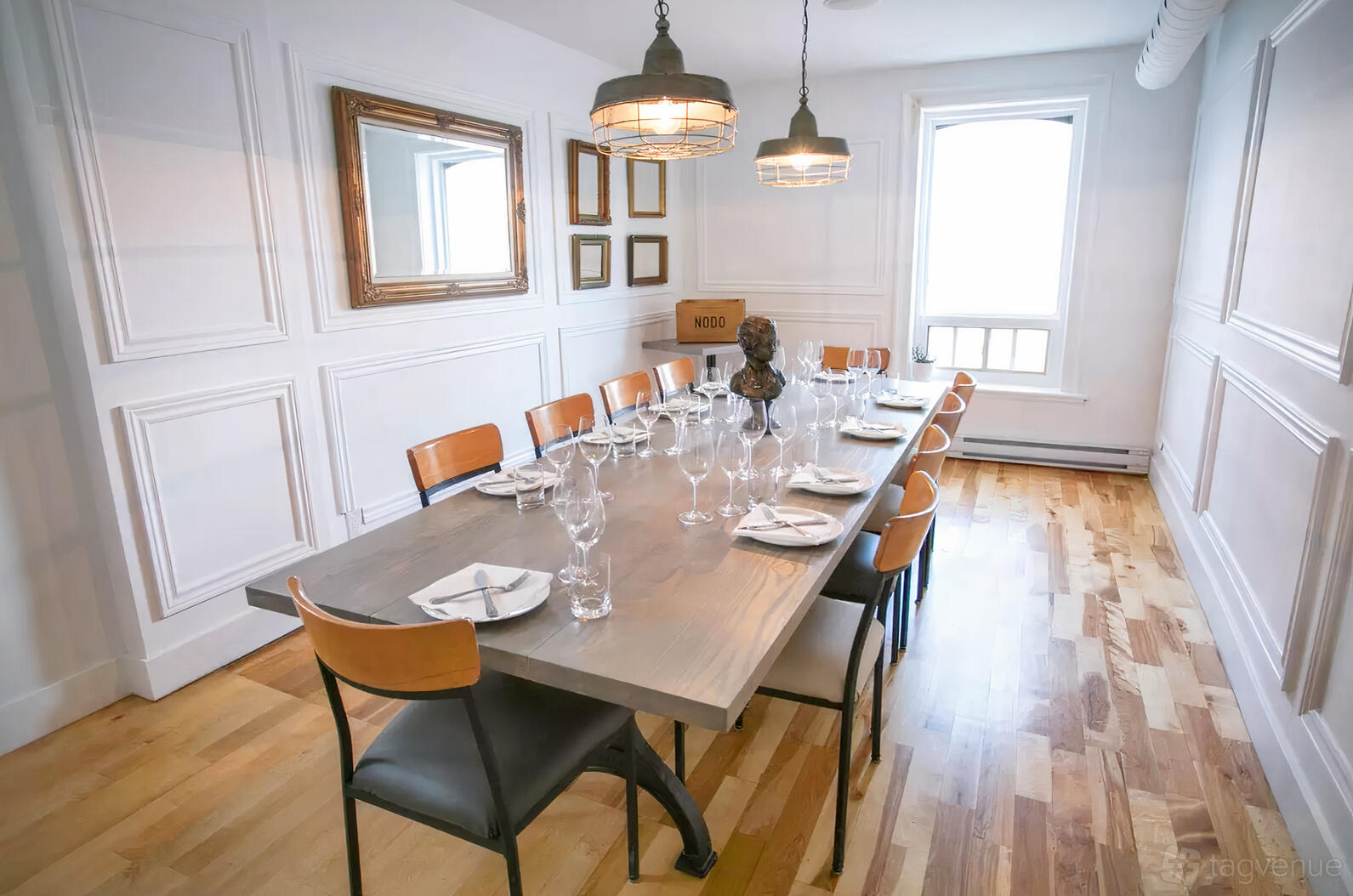 A dining room with a long wooden table set for twelve, leather chairs, and pendant lighting at Nodo Leslieville.