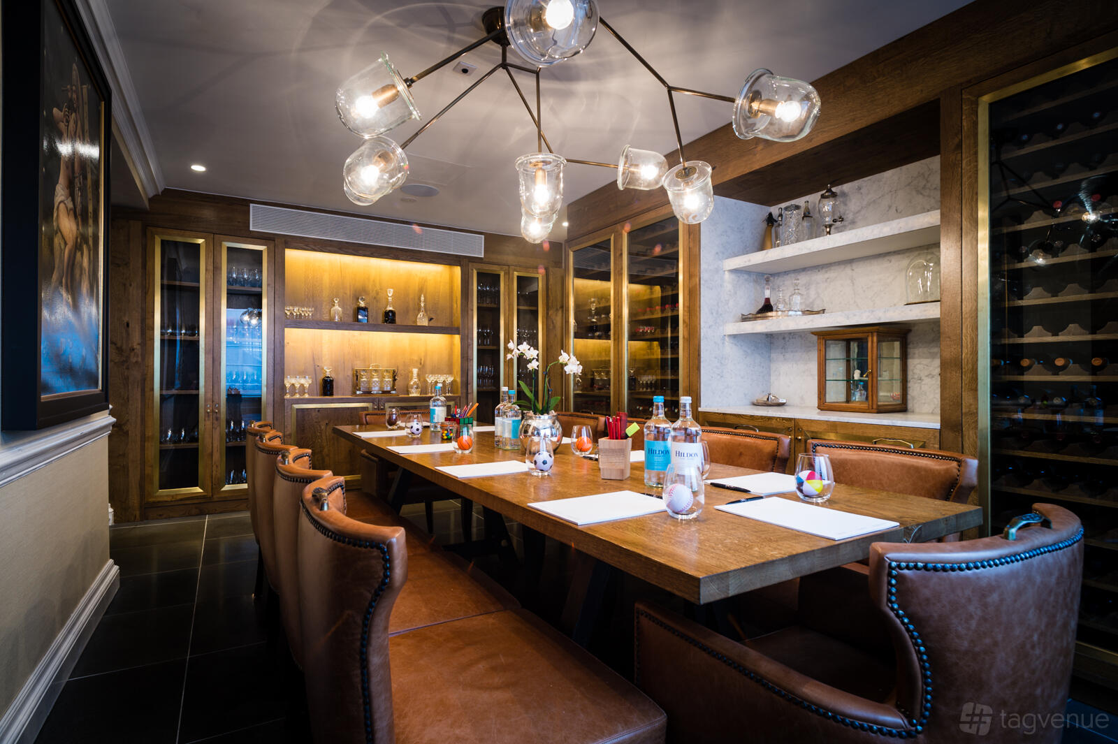 A dining room with leather chairs, long wooden table, and glass pendant lights at The Ampersand Hotel.