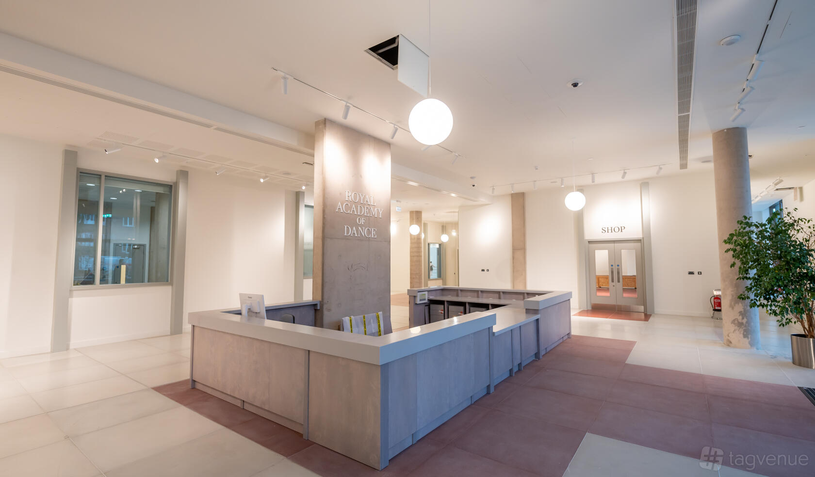 An office space reception with a wraparound front desk, pendant lighting, and a sign reading Royal Academy of Dance.