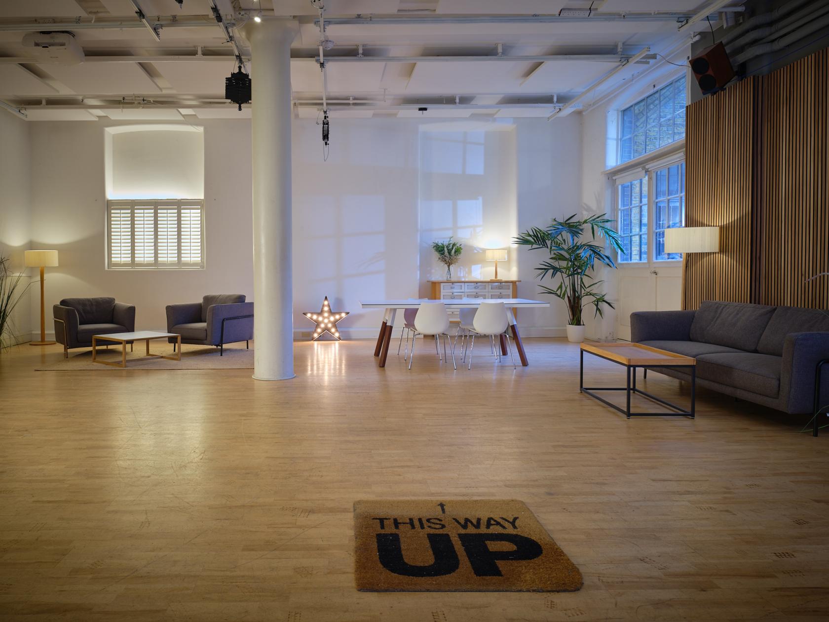 A photo studio with wood flooring, white walls, cozy lounge seating, and large windows at UP Studios.