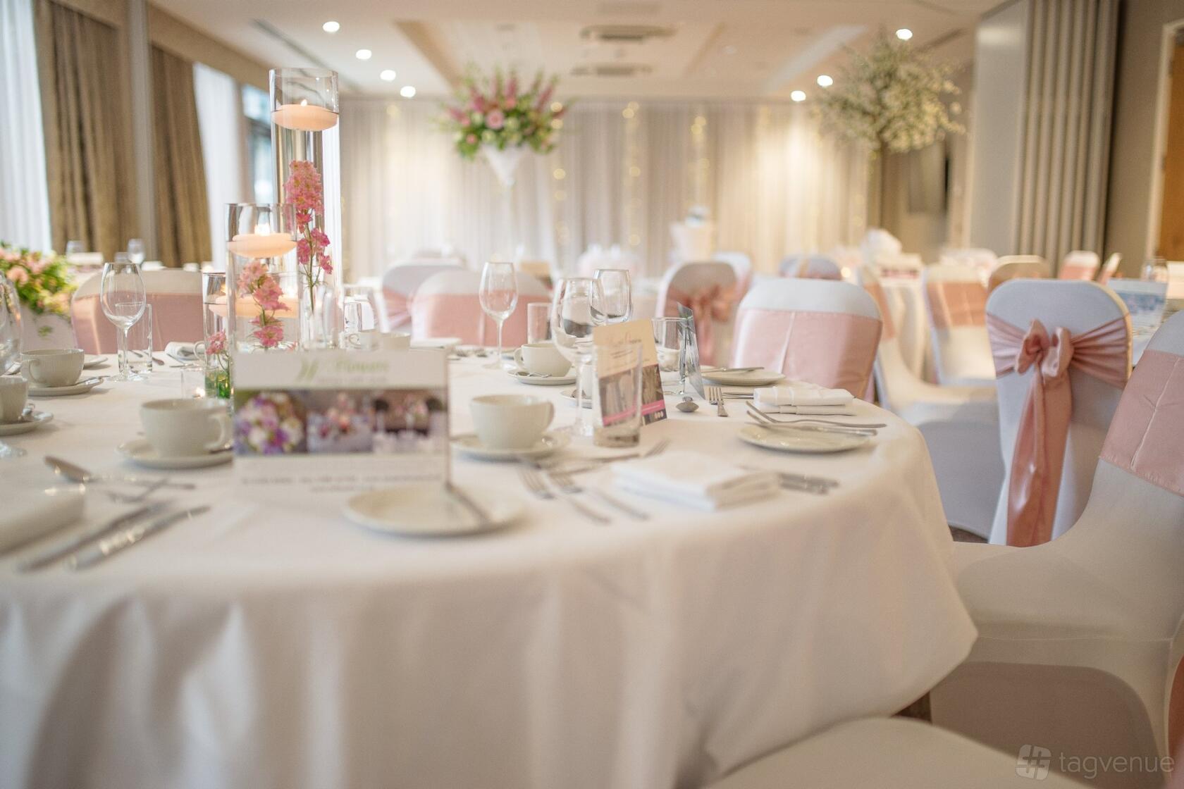 An event space with round tables set with white linens, glassware, and pink chair sashes at Wivenhoe House.