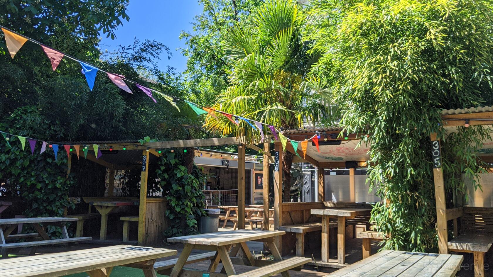 An outdoor pub garden with wooden picnic tables, colorful bunting, and lush greenery at People's Park Tavern.