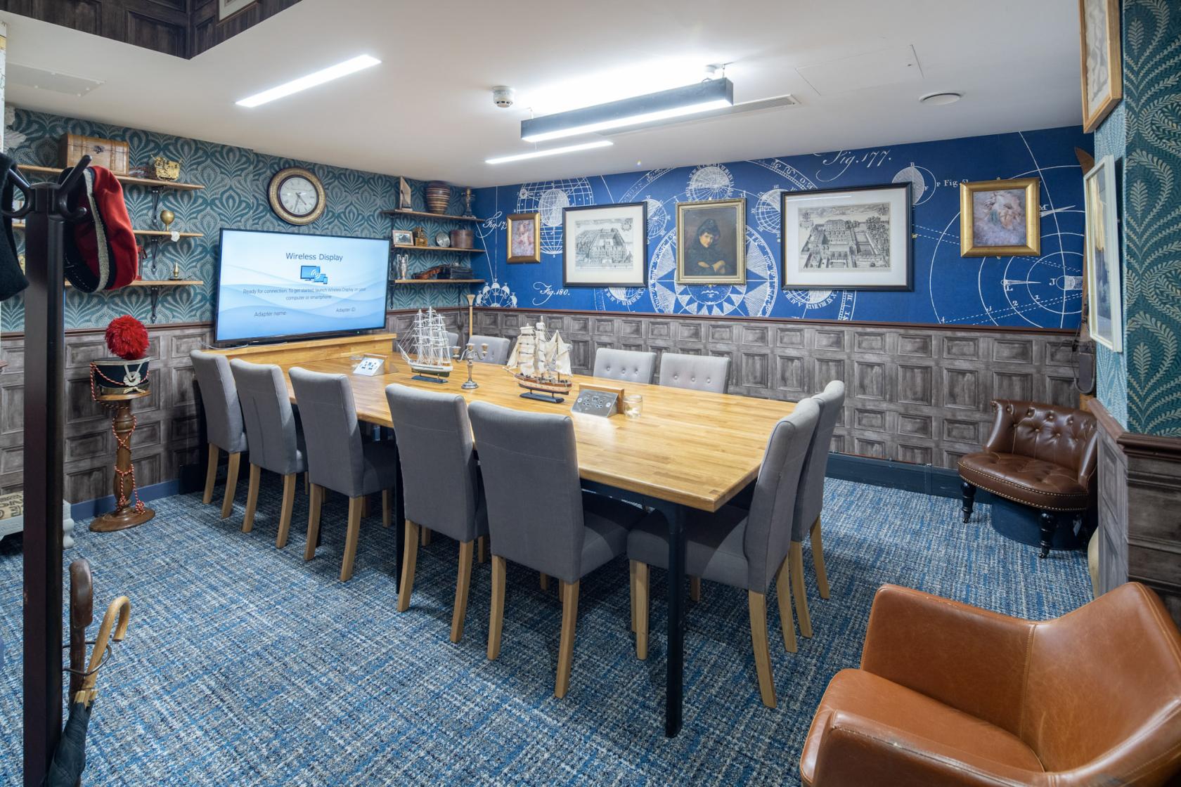 A boardroom with a long wooden table, cushioned chairs, nautical-themed decor, and framed maps at DeskLodge Beacon Tower Bristol.