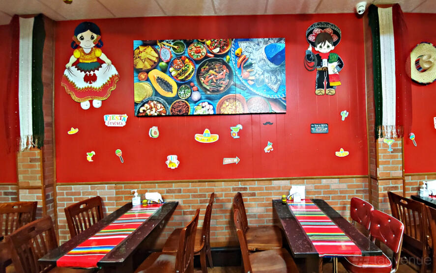 A restaurant dining area with wooden tables, striped table runners, red walls, and festive Mexican decor at Mexican Grill La Guera.