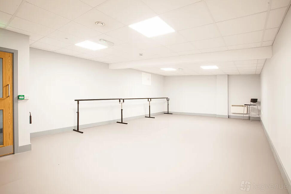 A dance studio with wall-mounted barres, white walls, and a light gray floor at Adagio School Of Dance.