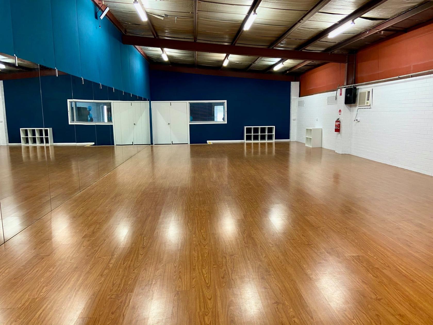 A rehearsal room with mirrored walls, wood flooring, and storage cubbies at National Performing Arts Company.