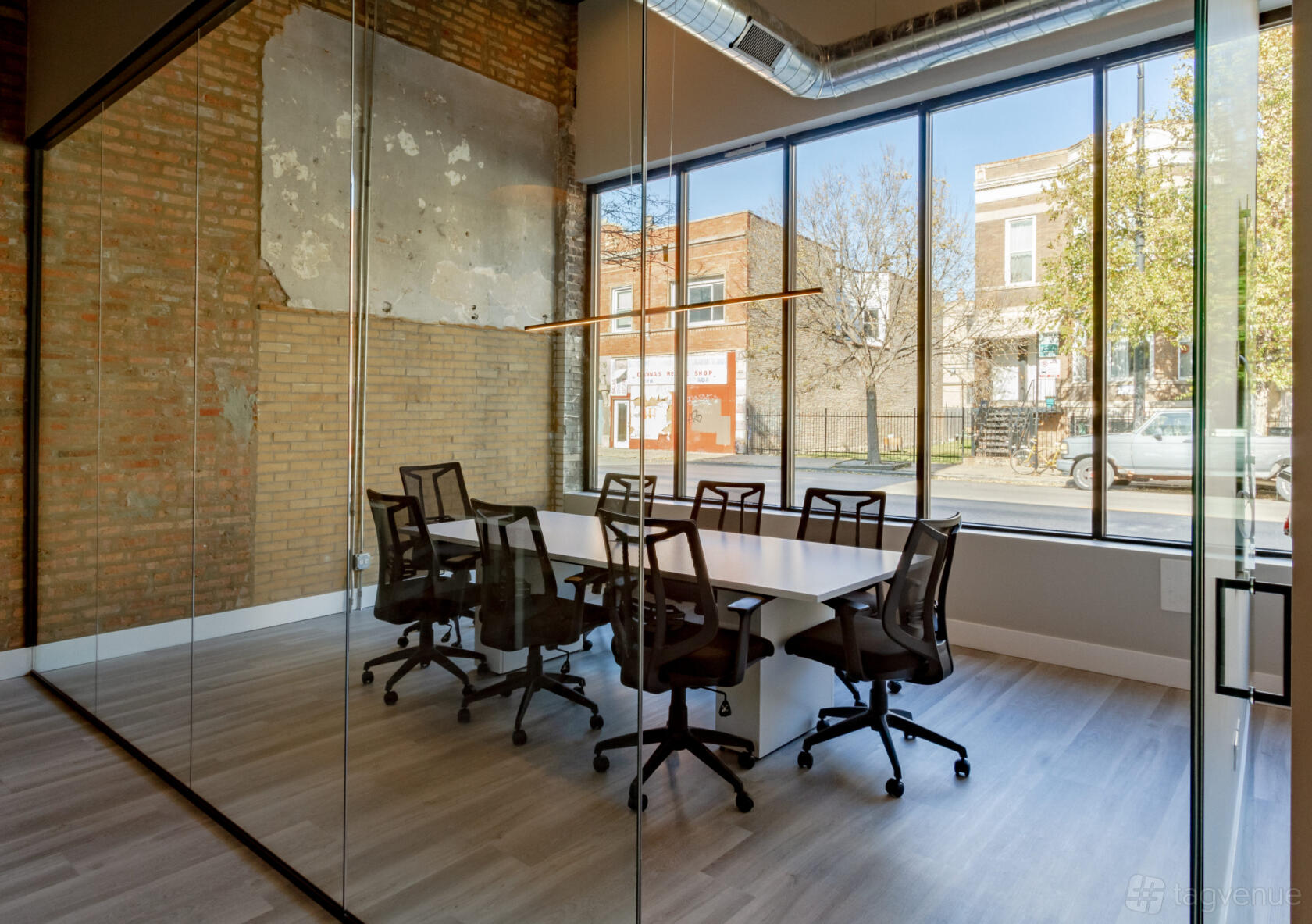 A meeting room with exposed brick walls, glass partitions, and a long table with black chairs at Desk 606.