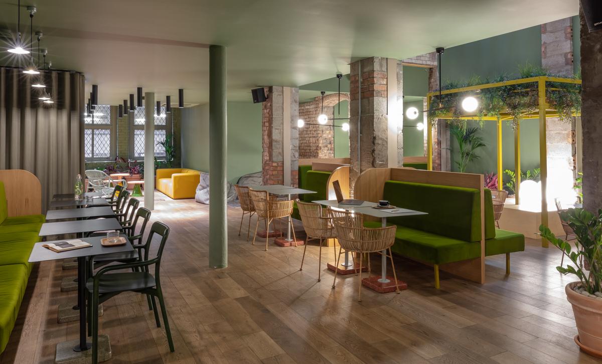 A hotel lounge with green booth seating, exposed brick columns, and light wood floors at Whitworth Locke Hotel Manchester.