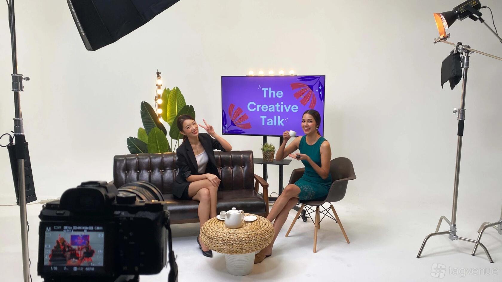 A photo studio with a talk show set, studio lighting, a sofa, and a backdrop with a TV screen at TVC Studio.