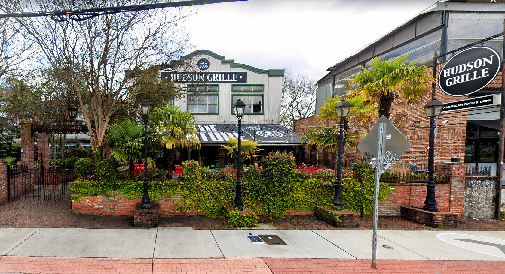A pub with a brick facade, outdoor seating, palm trees, and decorative lanterns at Hudson Grille - Little 5 Points.