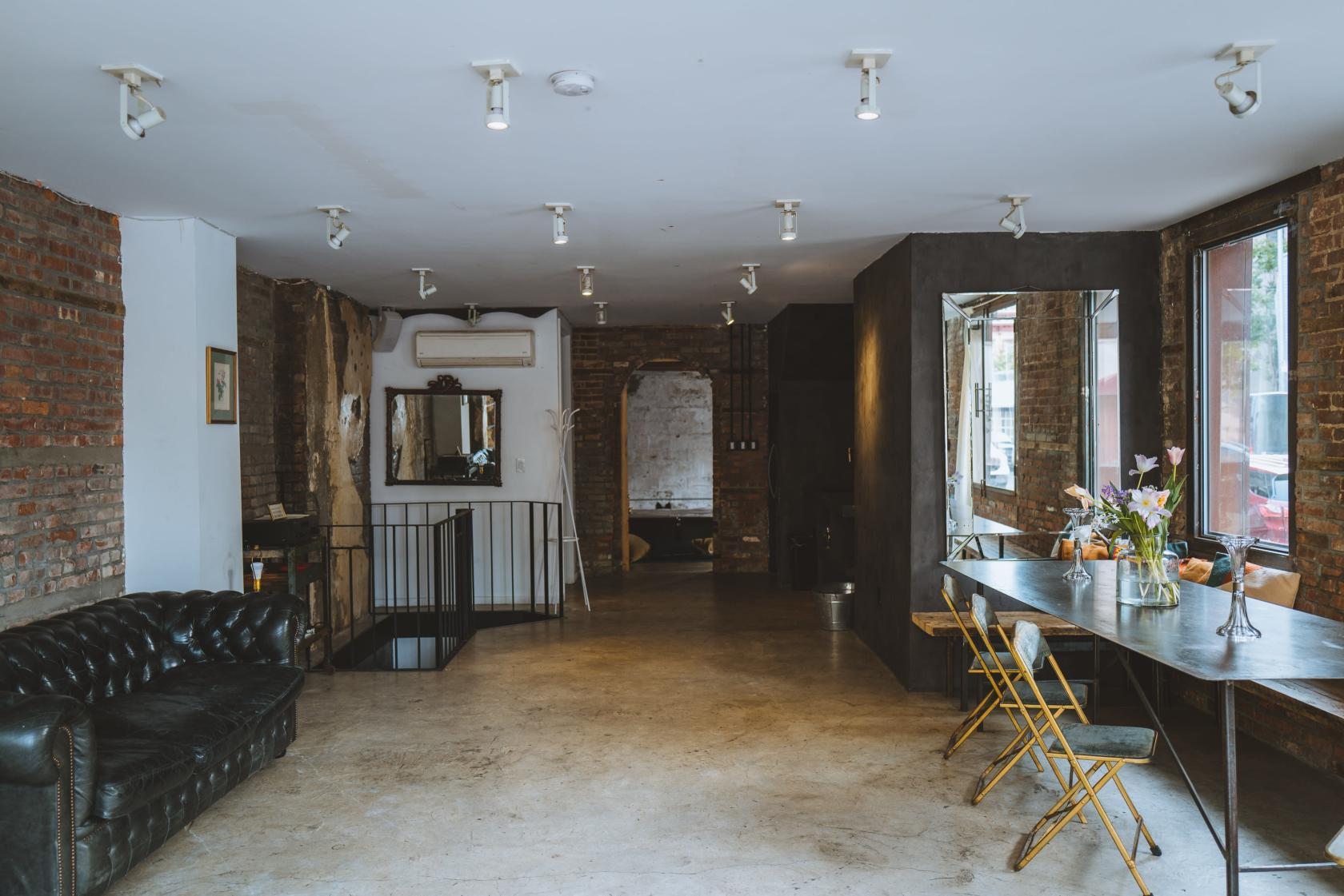 An event venue with exposed brick walls, concrete floors, and large windows with a long metal table at Rosa 402.