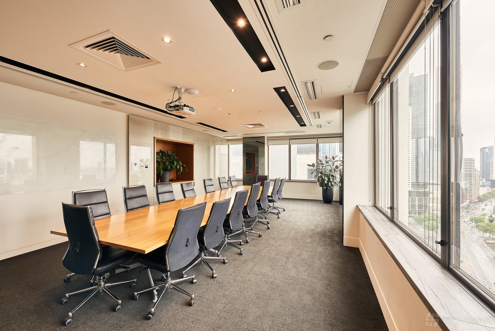 A boardroom with a long wooden conference table, black chairs, floor-to-ceiling windows, and city views at The Cluster.