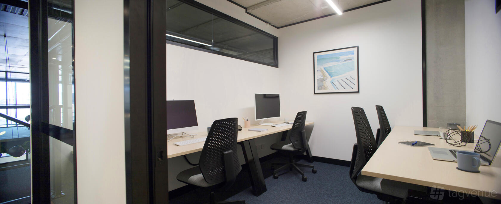 An office space with desks, black chairs, desktop monitors, and wall art at collective_100.