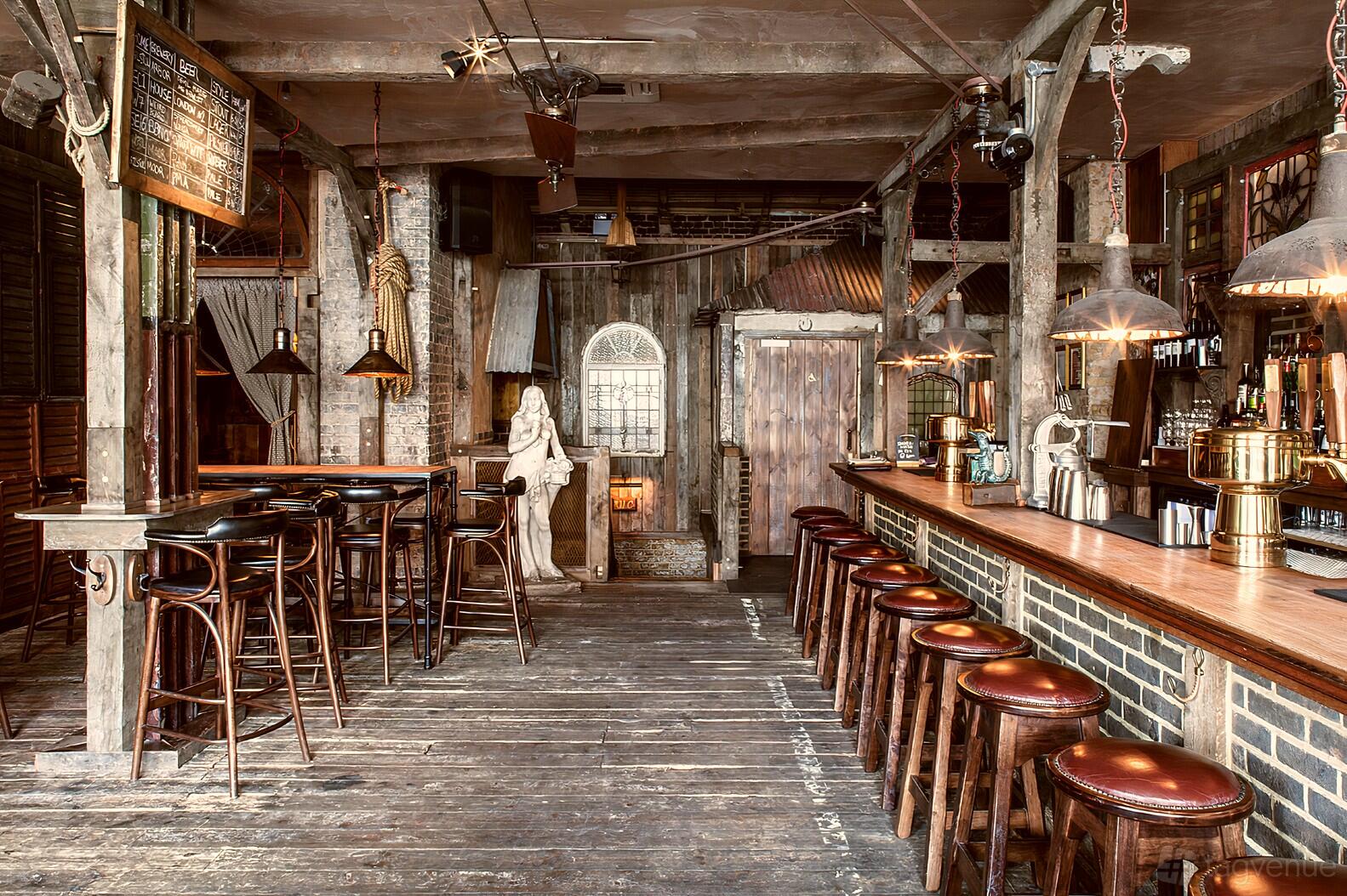 A rustic bar with wooden floors, exposed beams, round leather stools, and vintage decor at Ninth Ward London.