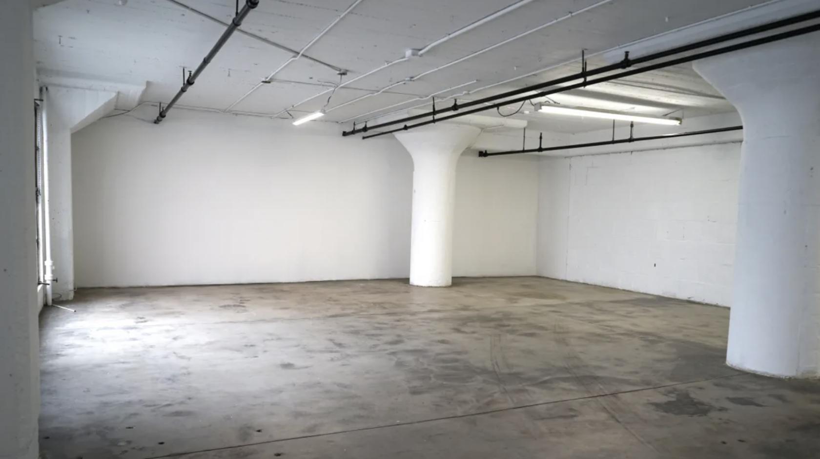 A photo studio with polished concrete floors, white walls, and exposed ceiling pipes at 1114 Studios.