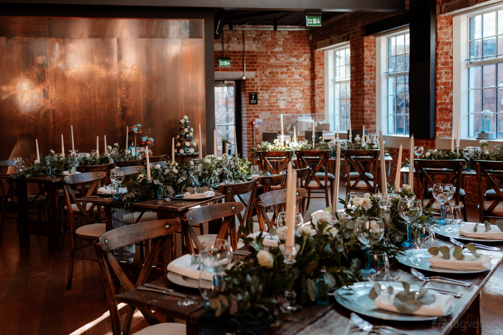A winery terrace with exposed brick walls, wooden tables set with white plates, candles, and greenery at Bombay Sapphire Distillery.