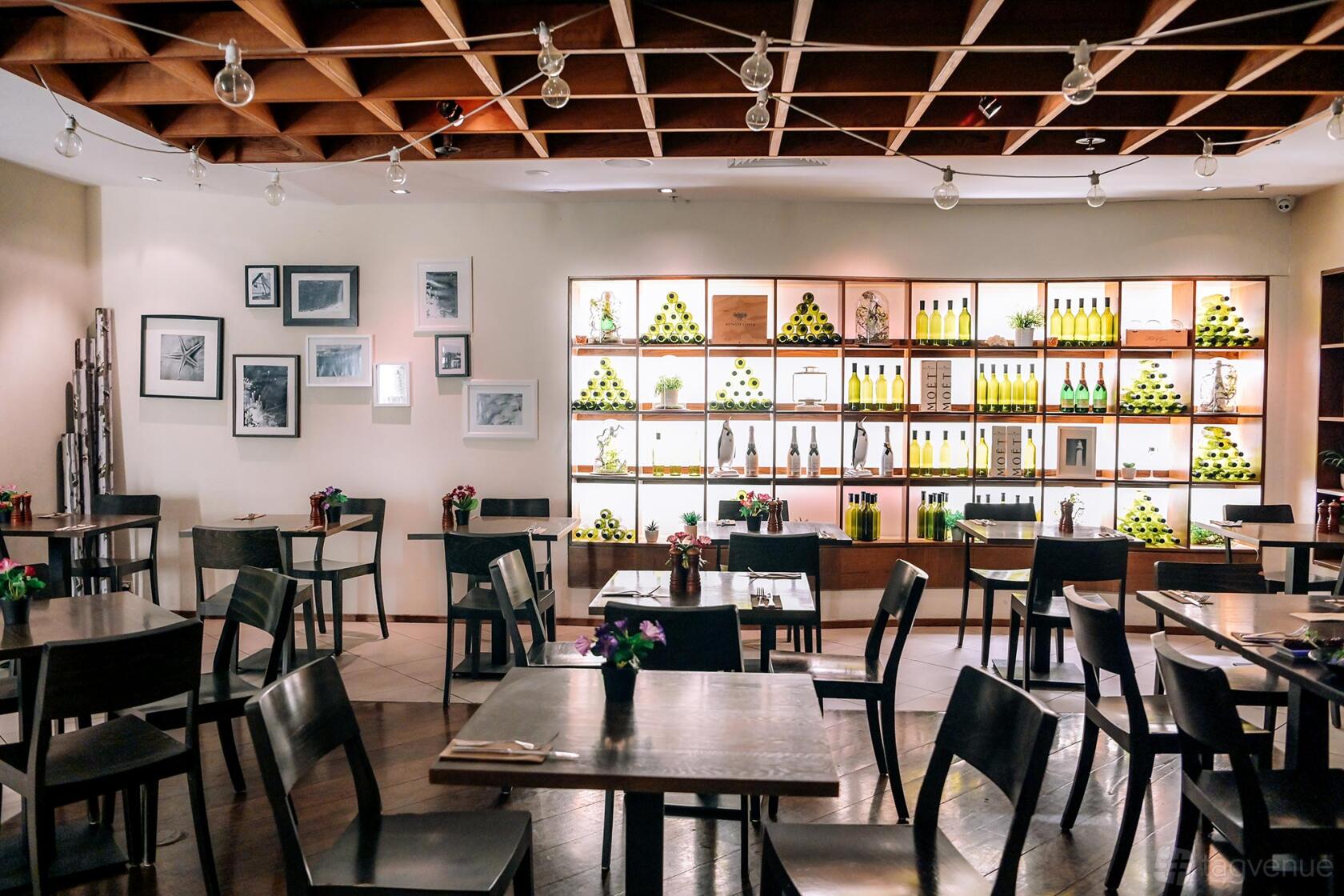 A restaurant function room with dark wood tables, framed wall art, and a backlit display of wine bottles at Searock Grill.
