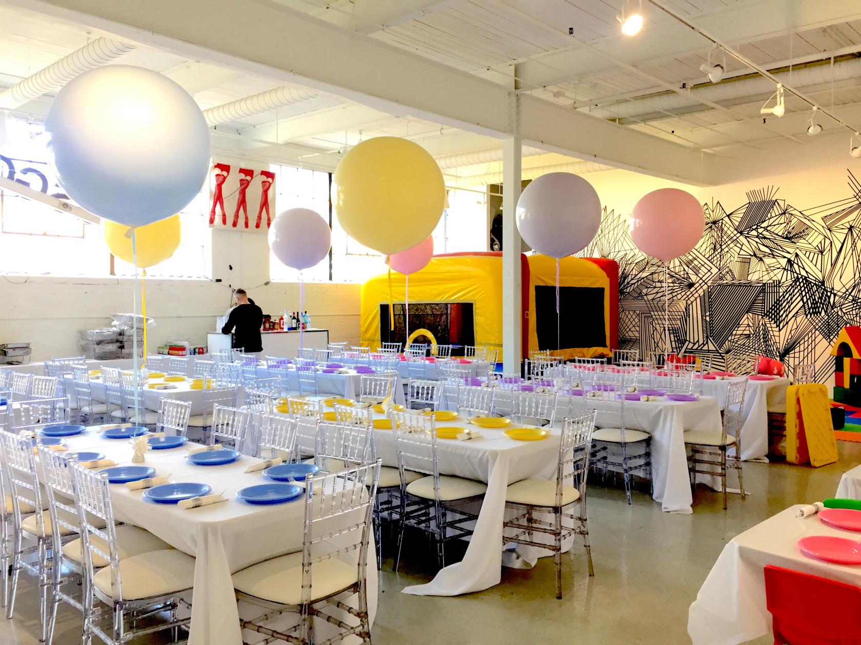 An event venue with long banquet tables, pastel balloons, and colorful plates at Jessica Gorlicky Designs.