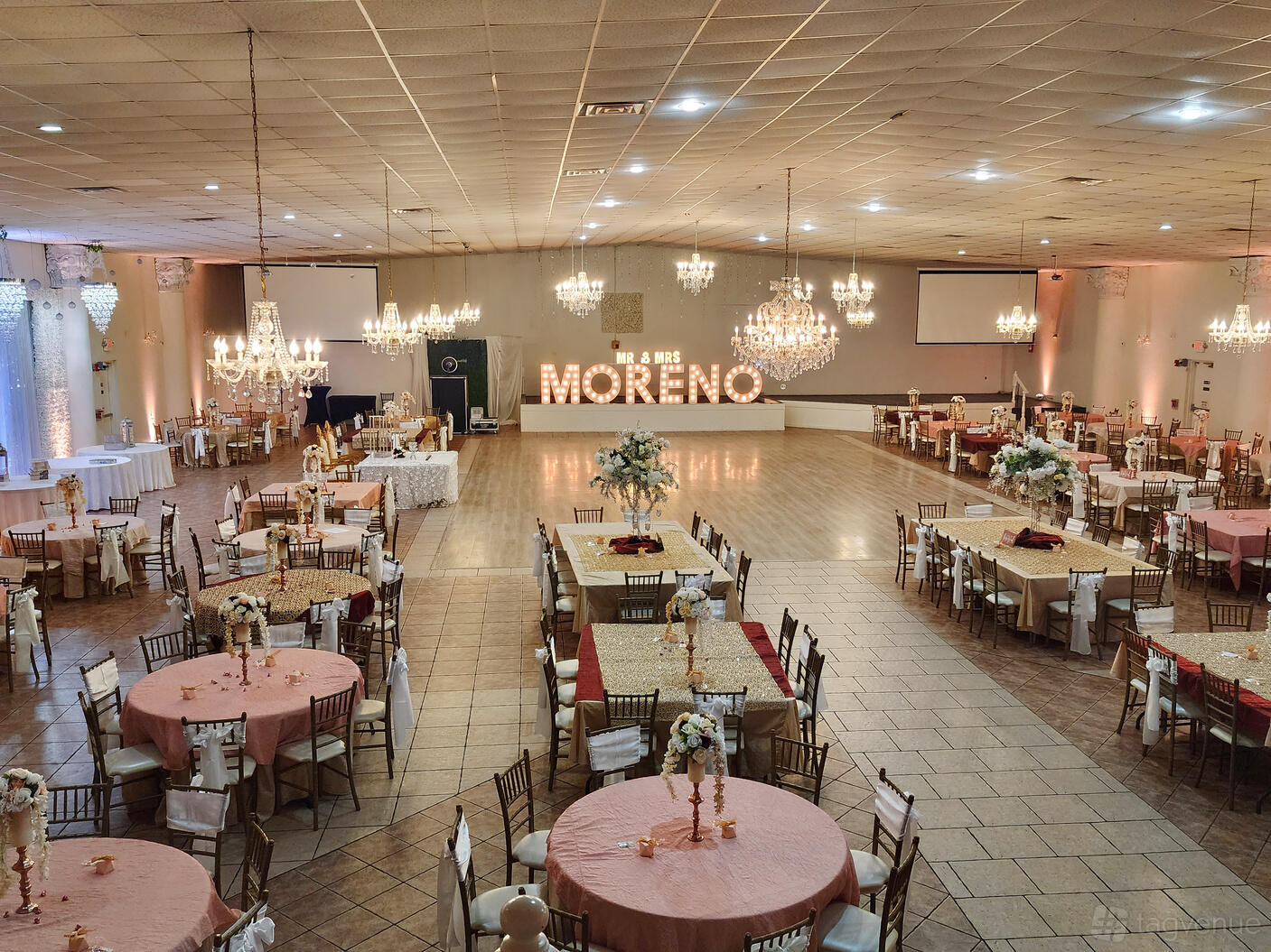 A spacious hall with chandeliers, a wooden dance floor, and decorated dining tables at Memories Reception Hall.
