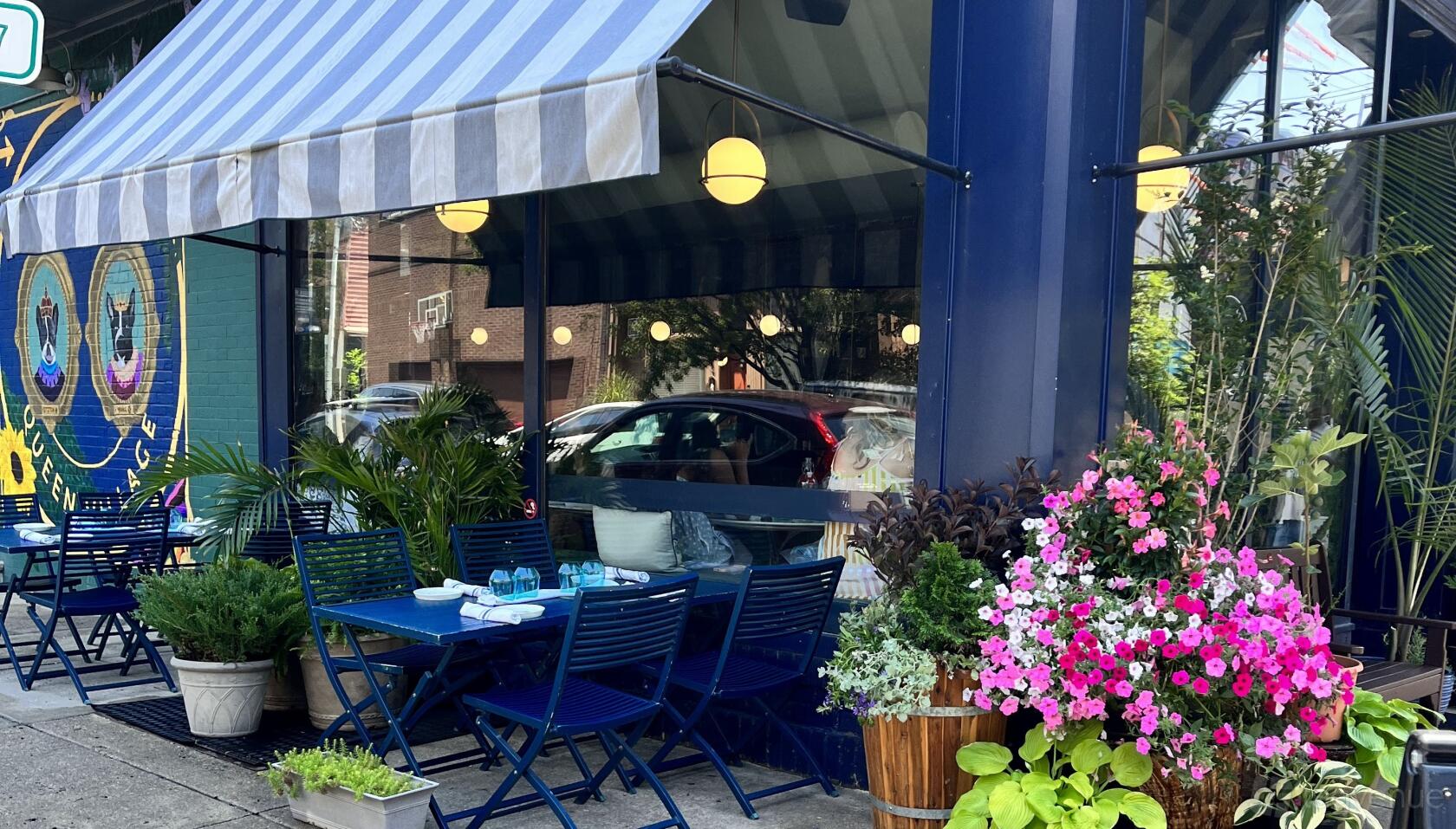An event space in a restaurant with blue outdoor seating, potted plants, and hanging globe lights at Fitz on 4th.