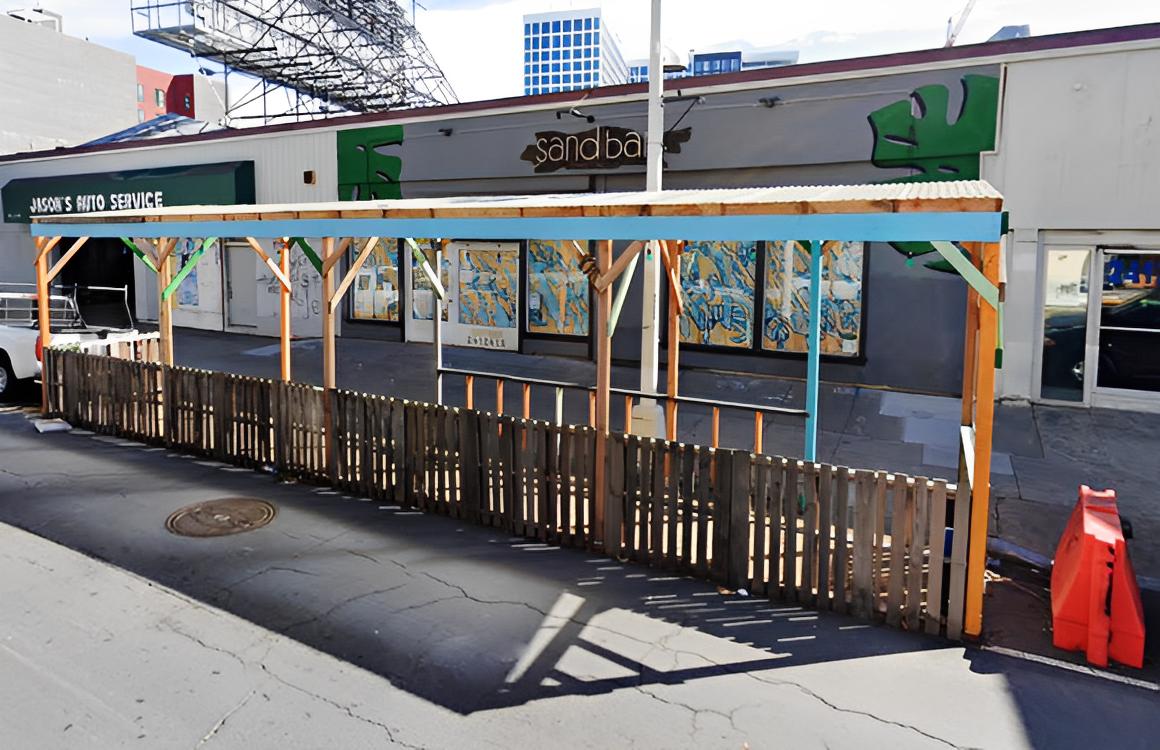 An outdoor bar area with a covered wooden parklet seating space and fenced perimeter at Sandbar.