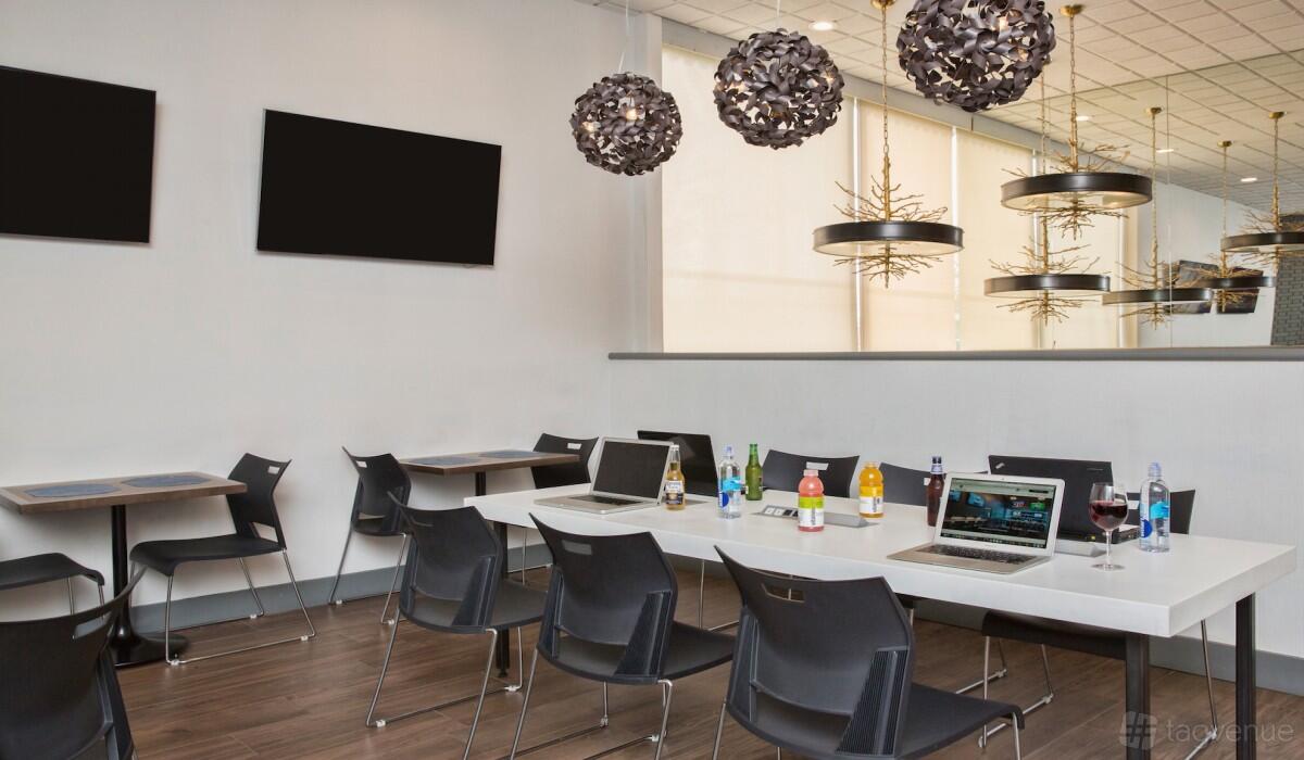 A boardroom with a long white table, black chairs, laptops, bottled drinks, and pendant lighting at Kenilworth Inn.