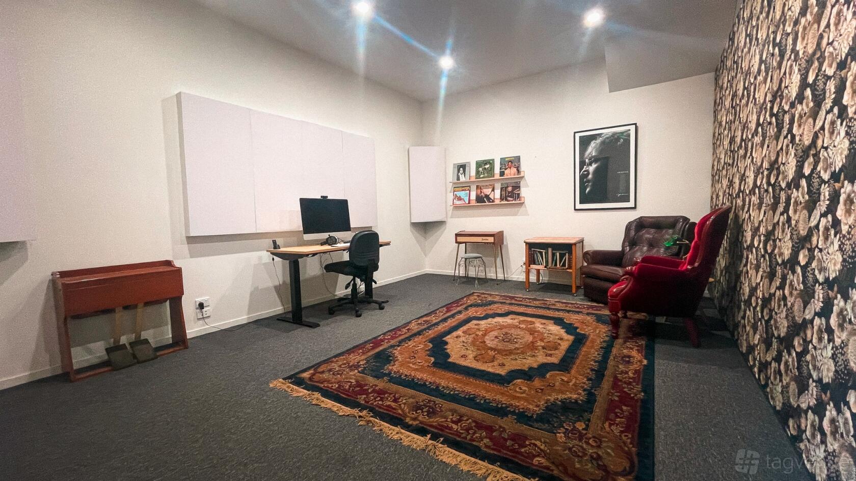 A recording studio office with a patterned rug, desk with computer, armchair, and decorative wall art at Elusive Creative.