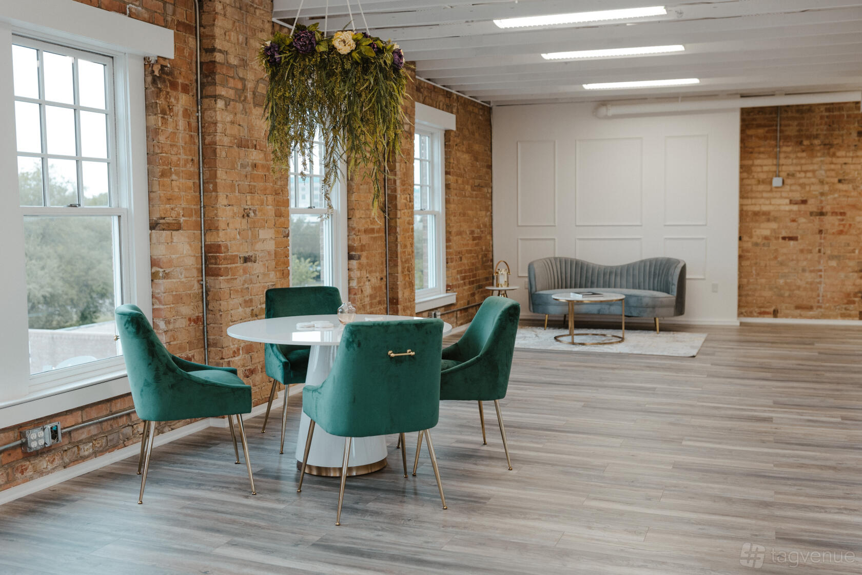 A photo studio with exposed brick walls, large windows, green velvet chairs, and a round table at IMSpaces.