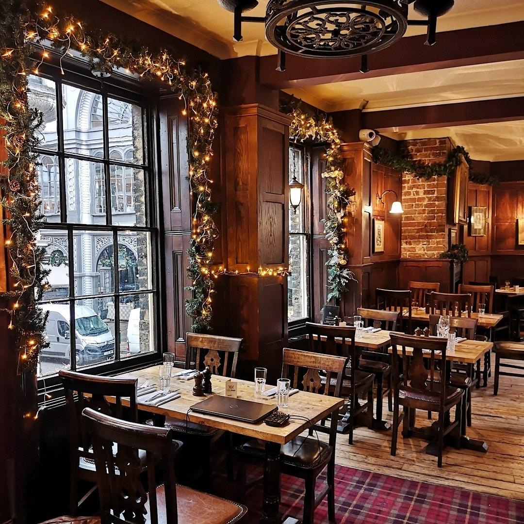 A function room in a pub with large windows, garland decorations, and wooden tables at The Market Porter.