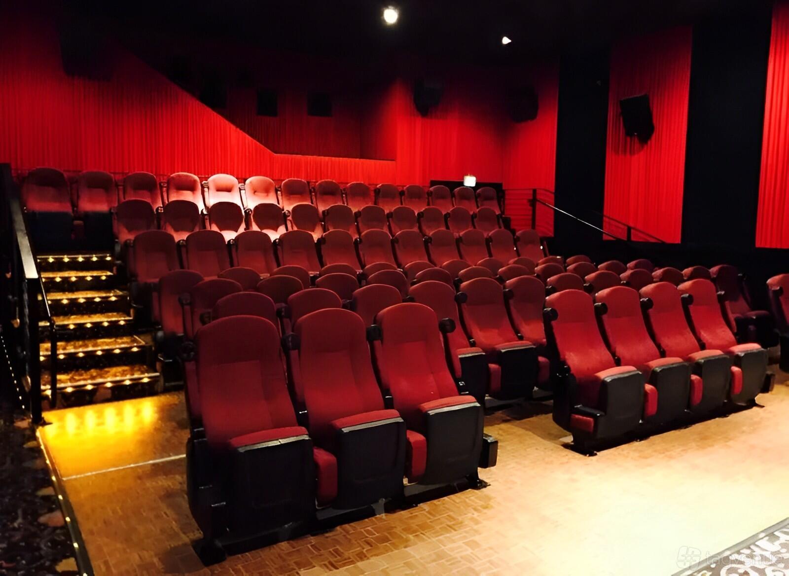 A cinema with tiered seating, red upholstered chairs, and illuminated aisle steps at Marina Theater.