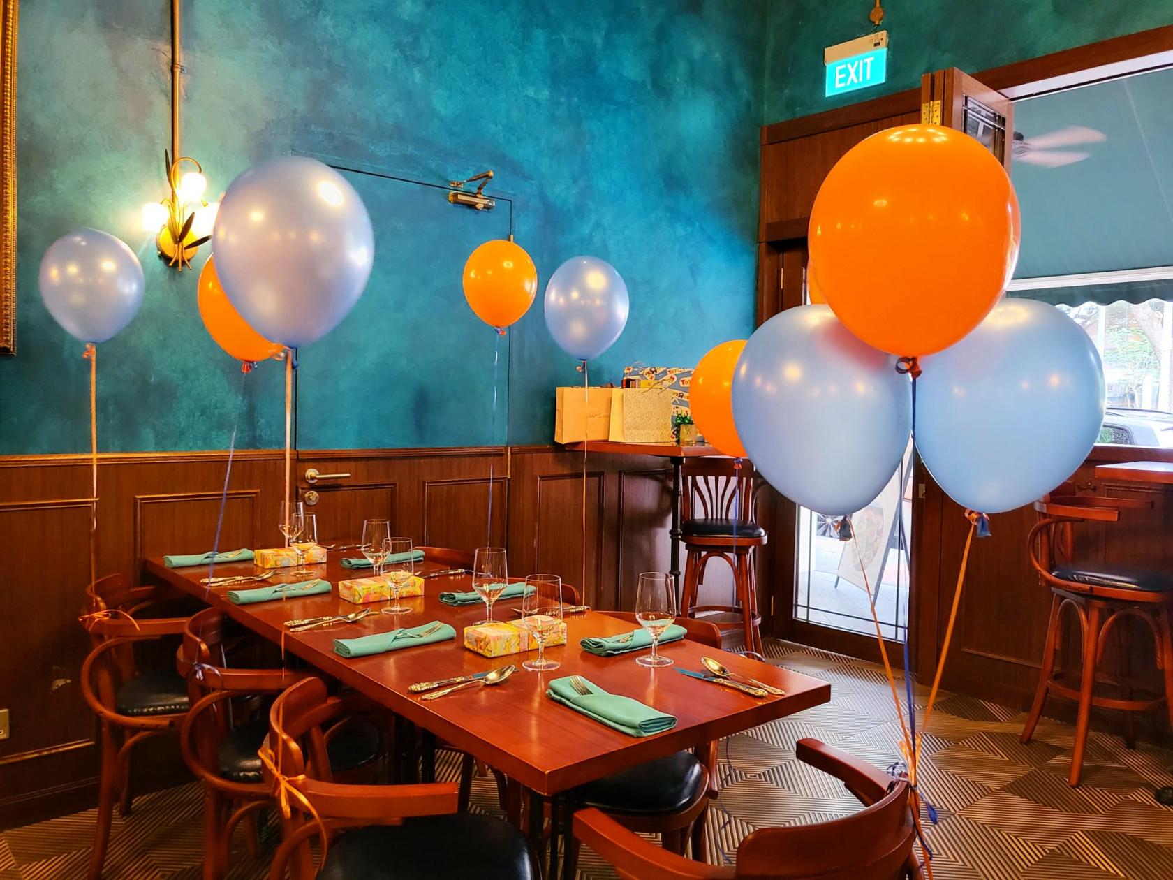 A restaurant with teal walls, wooden tables set with glassware, and orange and blue balloons at Quay House.