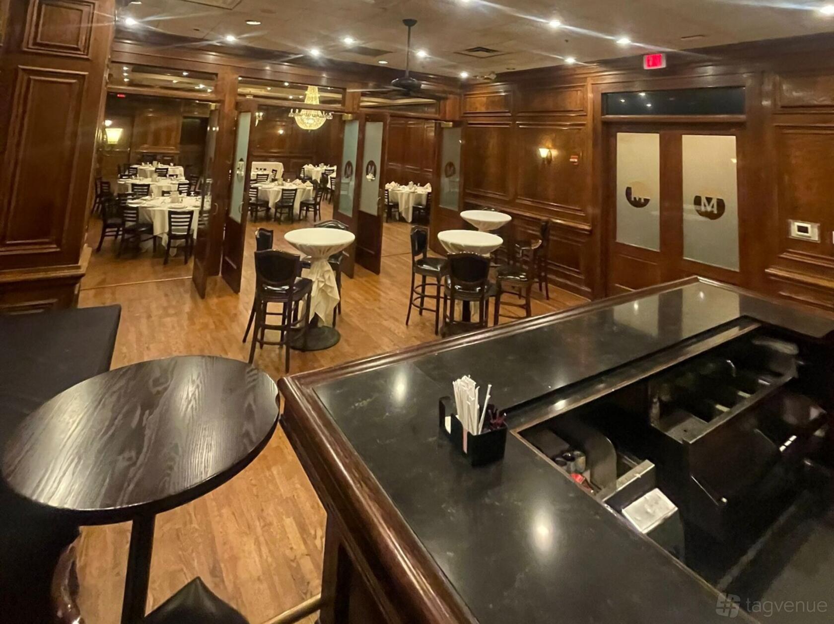 A wood-paneled bar with a polished black counter and round cocktail tables at Maggiano's Little Italy Chevy Chase.