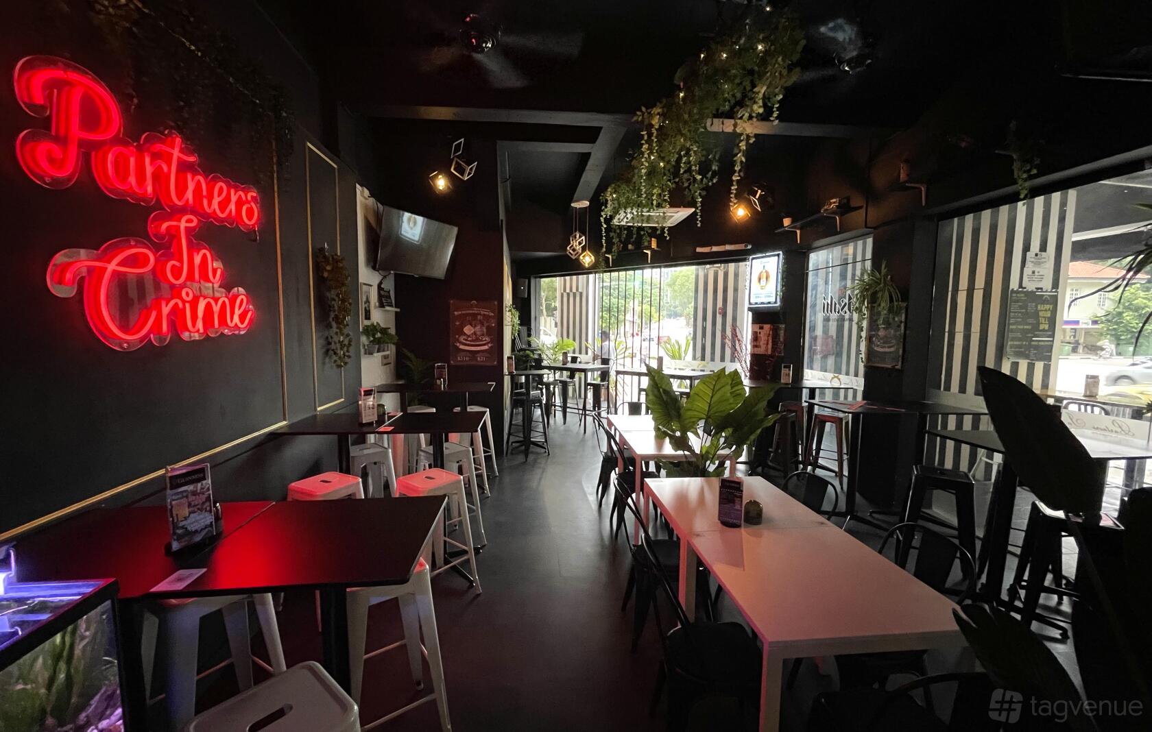 A restaurant with neon signs, high tables, black walls, hanging plants, and natural light at Partners In Crime.
