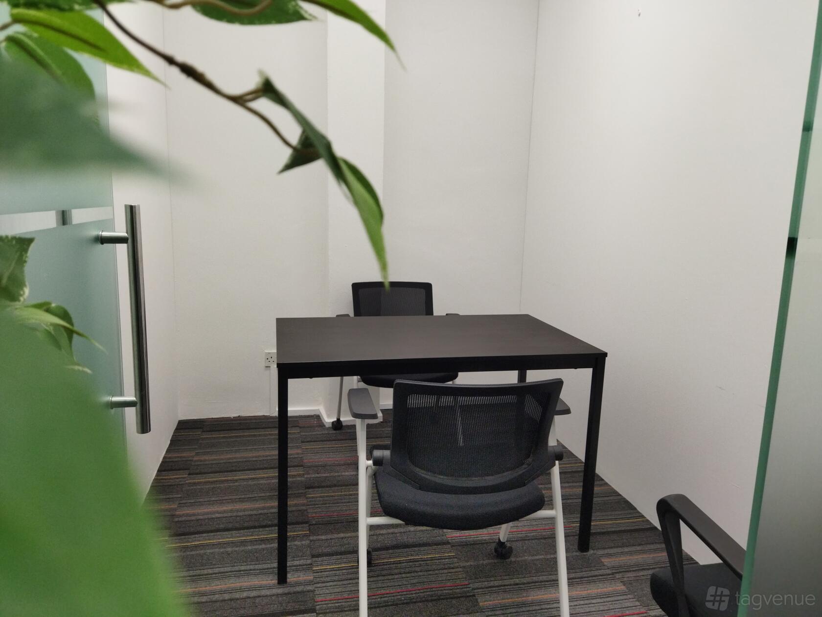 A meeting room with a black table, two office chairs, striped carpet, and white walls at Starich Studio & Office Rooms.