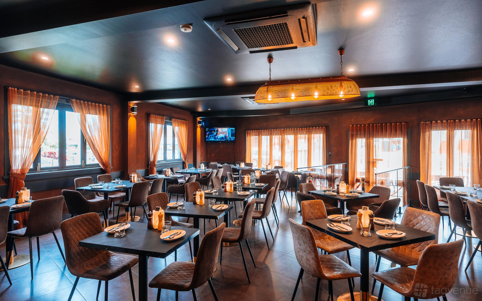 A restaurant with floor-to-ceiling windows, warm lighting, and neatly set square tables at Elements Bar & Grill Haberfield.