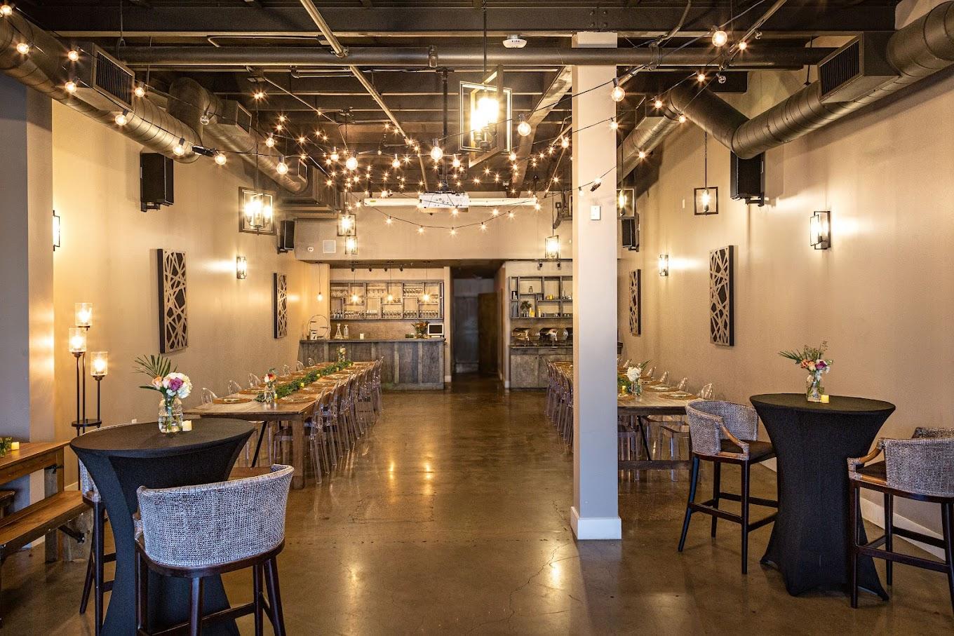 An event venue with string lights, long wooden tables, and a polished concrete floor at The 77.