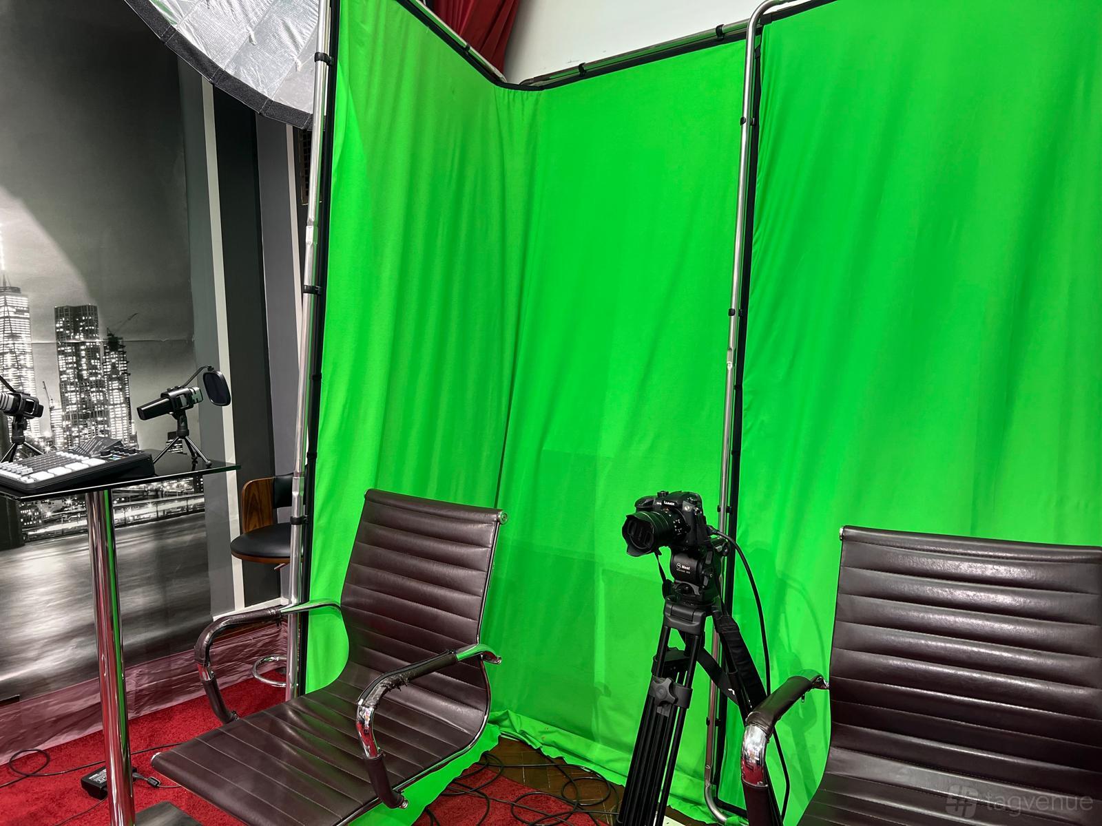 A photo studio with a green screen backdrop, two brown chairs, a tripod camera, and studio microphones at Millmead Business Centre.