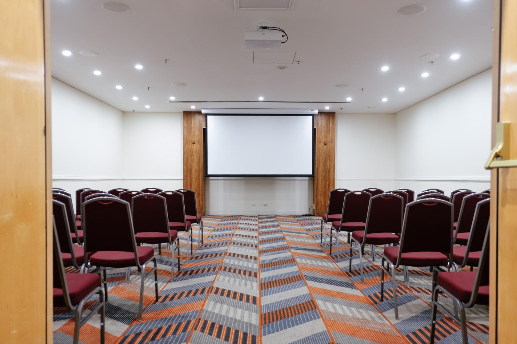 An event space with patterned carpet, rows of burgundy chairs, and a projection screen at Sydney Central Hotel.