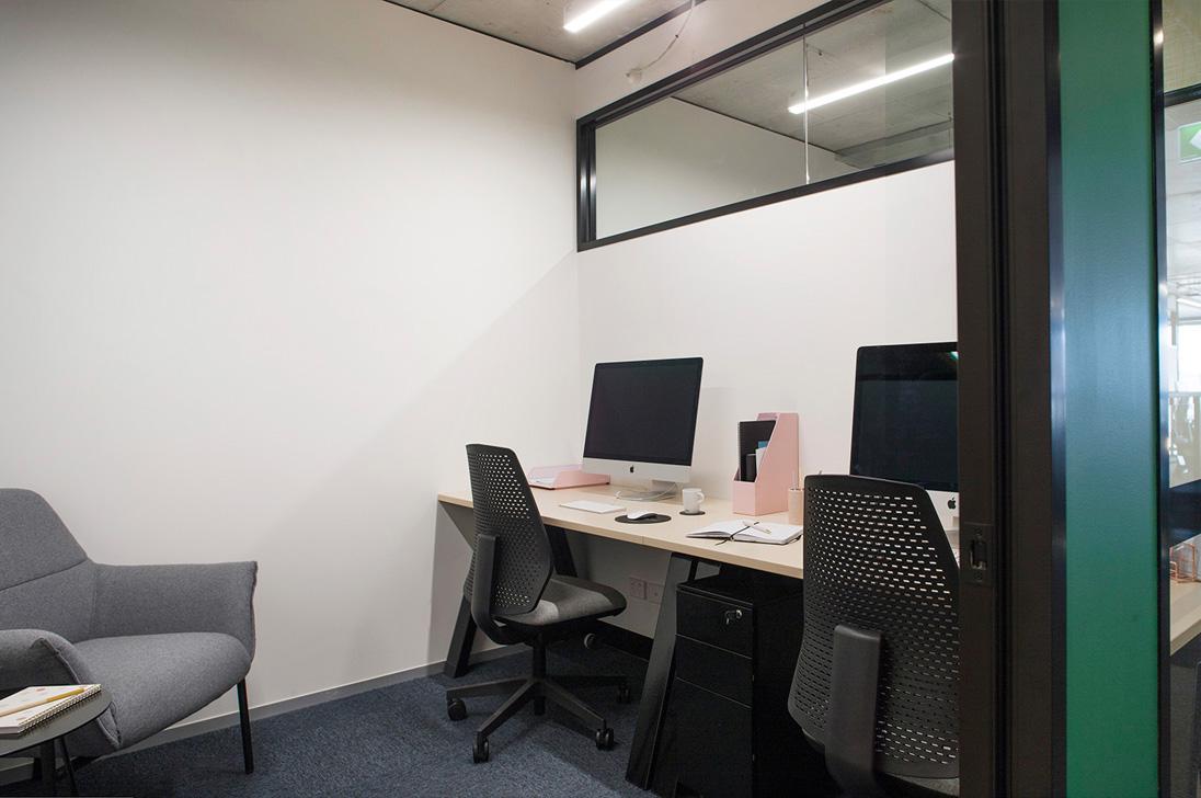 An office space with two workstations, desktop computers, and a gray armchair at collective_100.