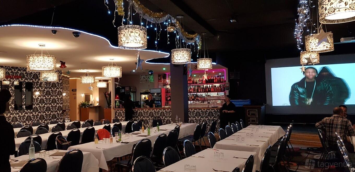 A restaurant with chandeliers, patterned walls, long tables with white linens, and a backlit bar at River Canyon Venue & Function Centre.