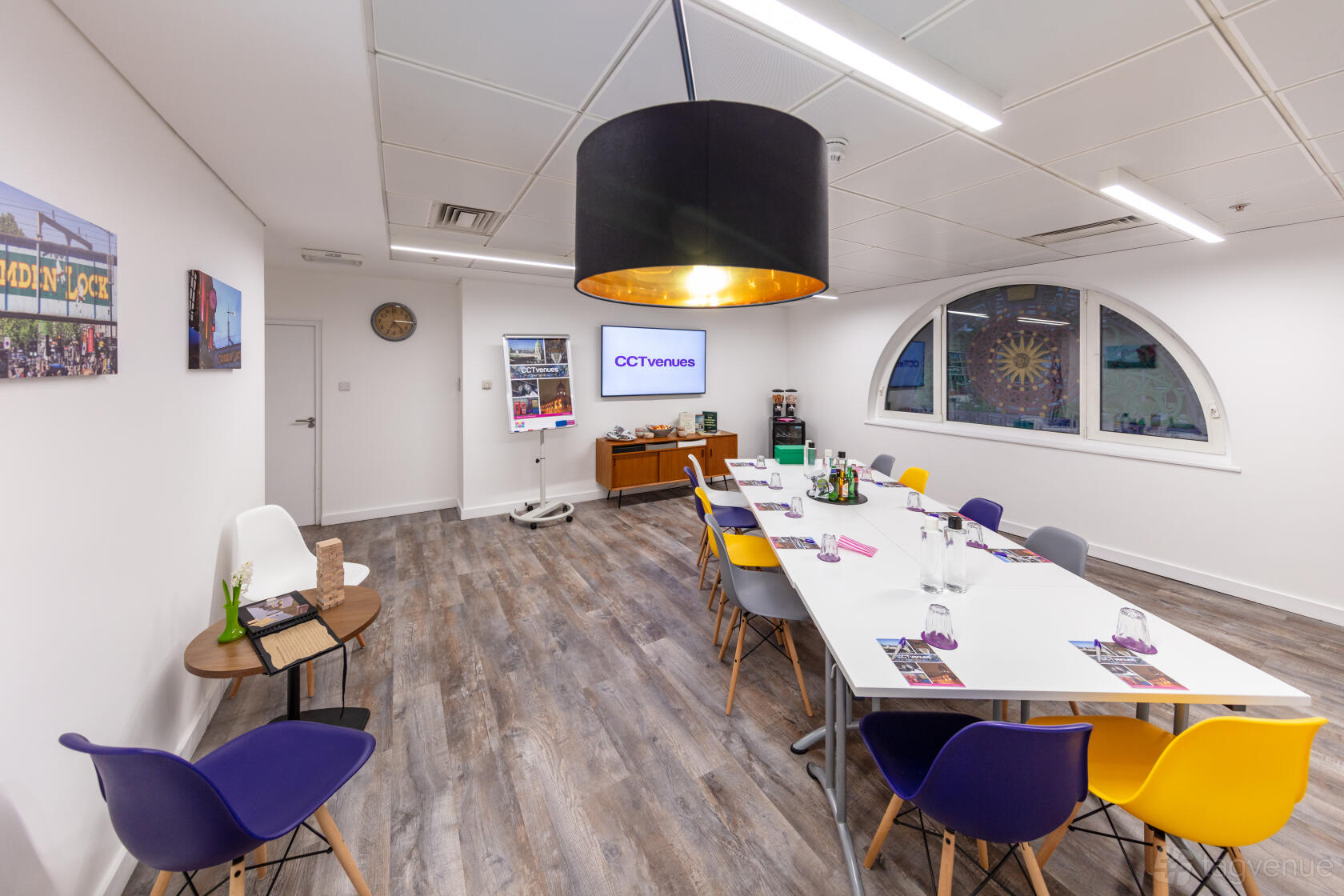 A conference centre room with a long meeting table, colorful chairs, and arched window at CCT Venues - Smithfield.