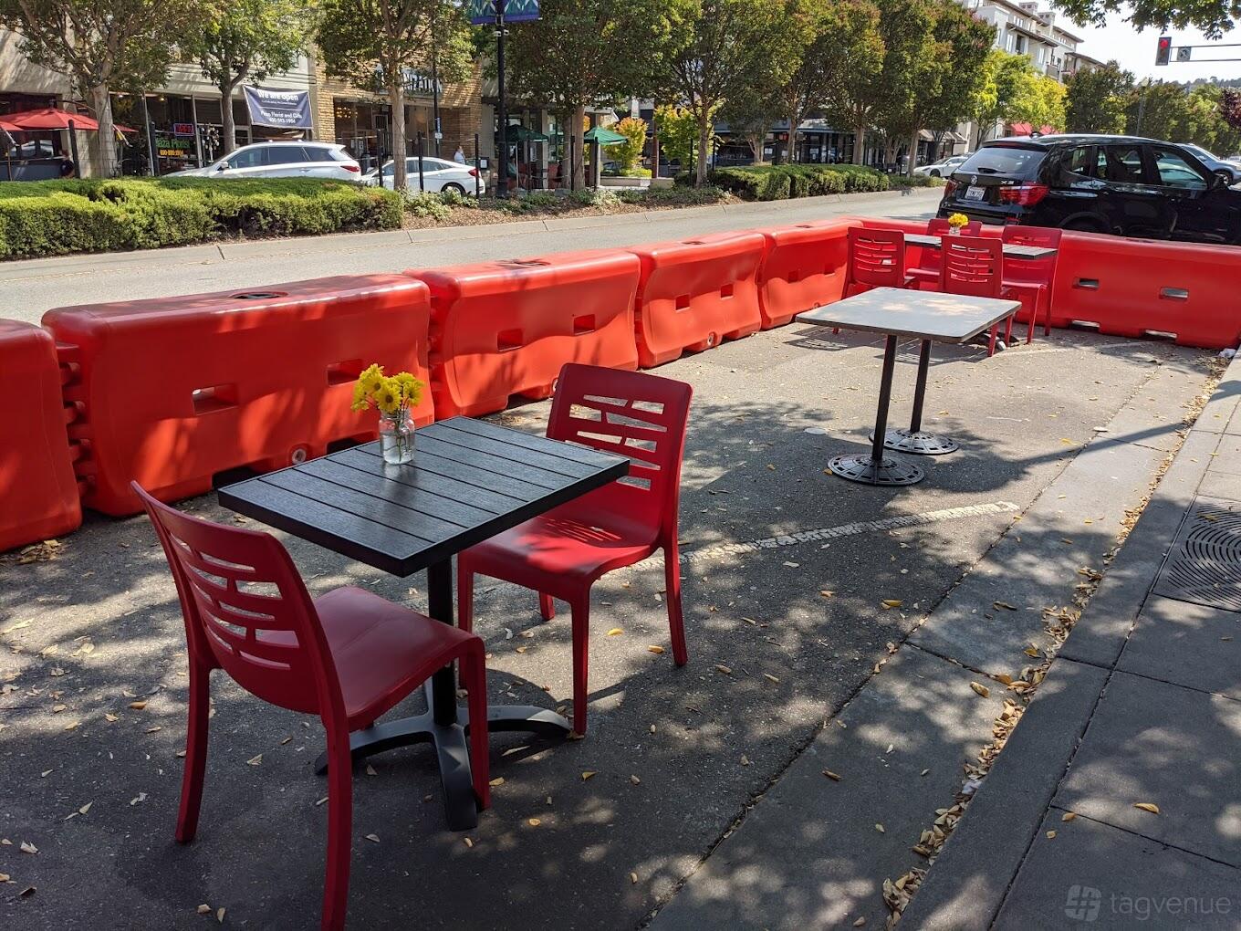 An outdoor restaurant patio with red chairs, small square tables, and yellow flower centerpieces at Tamari Authentic Georgian Cuisine.