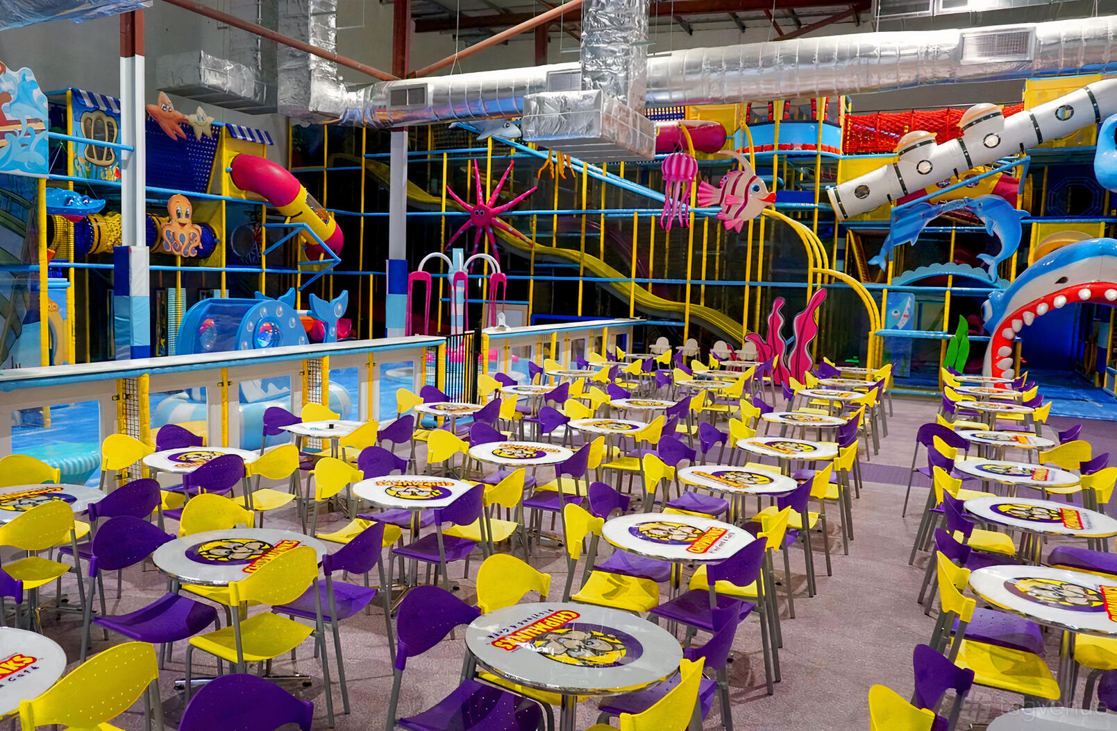 An event venue with rows of colorful tables and chairs beside an indoor playground at CHIPMUNKS BALLARAT.
