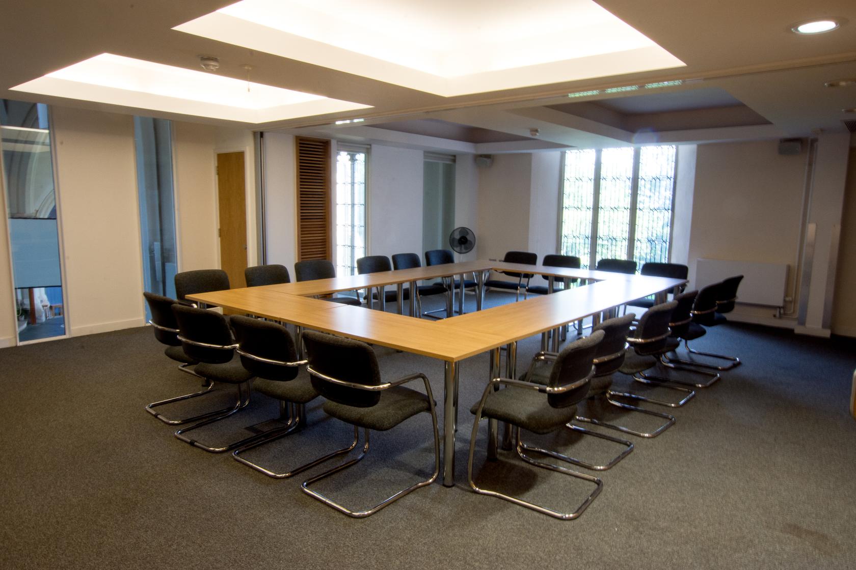A meeting room with a U-shaped conference table, black chairs, and carpeted floor at St Barnabas Church Centre.
