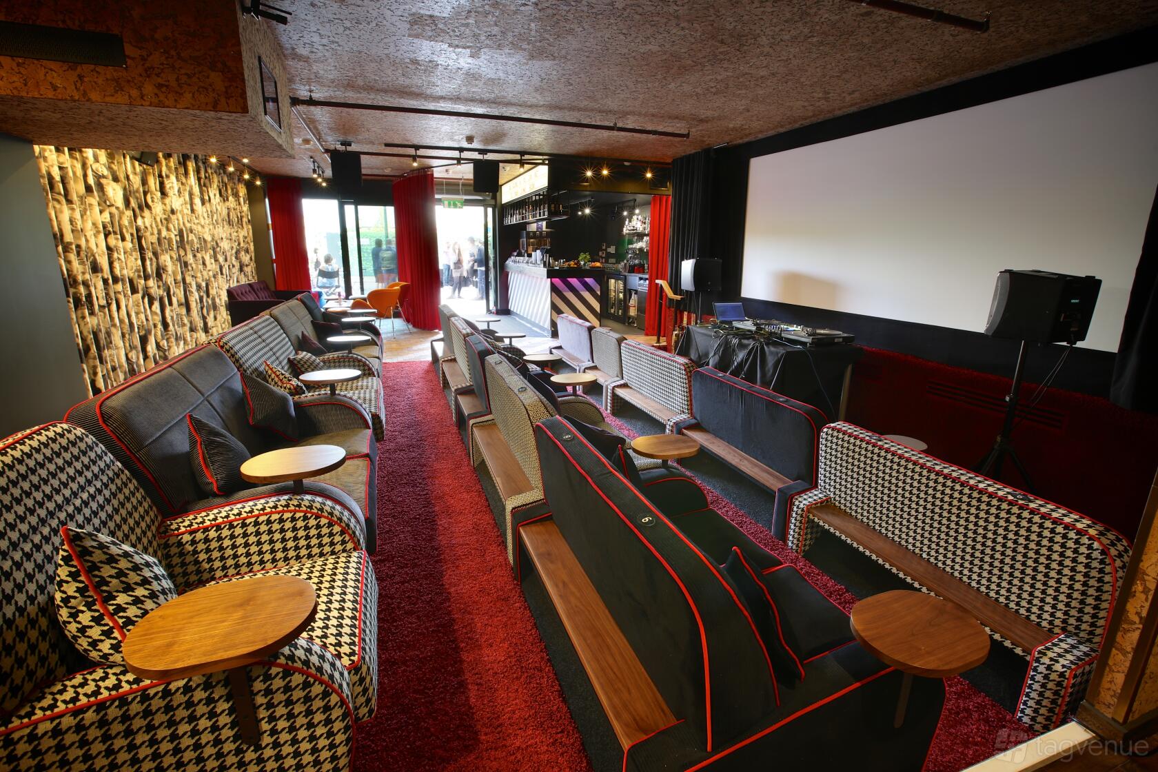 A cinema lounge with houndstooth sofas, red carpeting, and a large projector screen at Everyman Kings Cross.