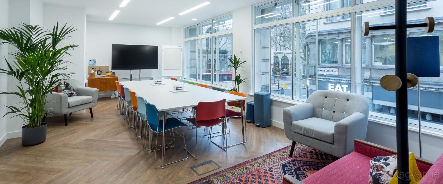 A creative space with floor-to-ceiling windows, colorful chairs, and a large screen at Wallacespace Covent Garden - 53 Parker Street.