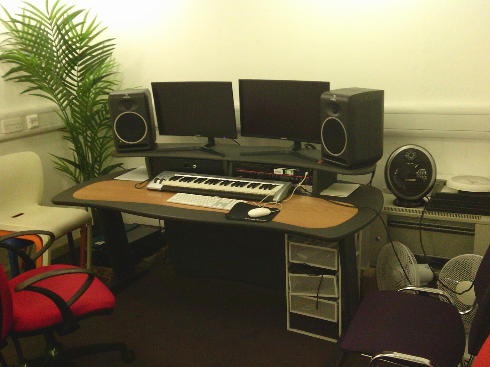 A recording room with dual monitors, studio speakers, a keyboard, and a potted plant at Collective Acting Studio.